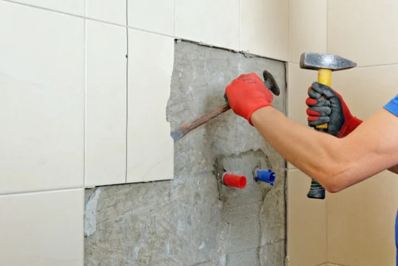 Person entfernt Fliesen mit Hammer und Meißel.